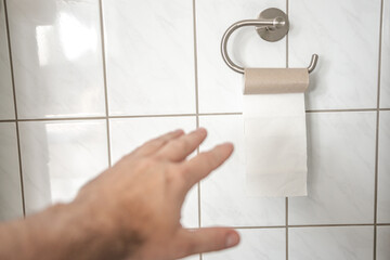 Man hand is trying to take last piece of toilet paper roll in the bathroom, closeup, details.
