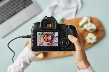 Top view close up of food photographer holding digital camera with image on screen while working in home studio, copy space - obrazy, fototapety, plakaty