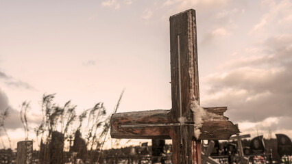 Snowy old broken grave wooden cross shaped on dramatic sky background. Orthodox traditional cemetery in snowy winter.