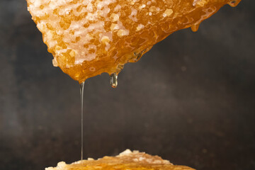 Honeycomb, textured with Golden organic honey, in sunlight, on black background. Drops of honey...