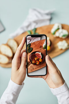 Minimal top view of young woman taking aesthetic photo of food using smartphone in home studio