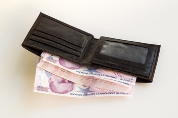 Brown leather men's wallet, fully loaded with Turkish two-hundred banknotes, on a white surface
