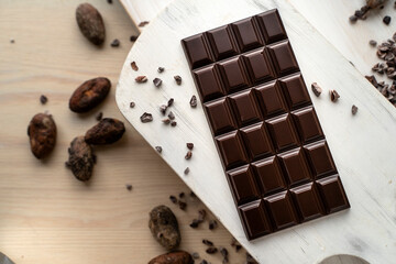 Dark bitter chocolate bar with cocoa beans on a wooden white background, top view. delicious chocolate. Space for text
