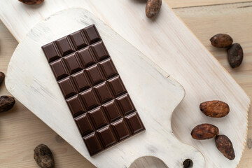 Dark bitter chocolate bar with cocoa beans on a wooden white background, top view. delicious...