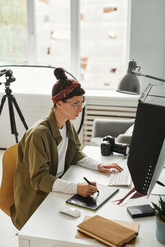 High angle portrait of young female photographer using computer while editing photos in studio