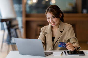 Young beautiful Asian woman using credit card and laptop for online shopping at outdoor park,...