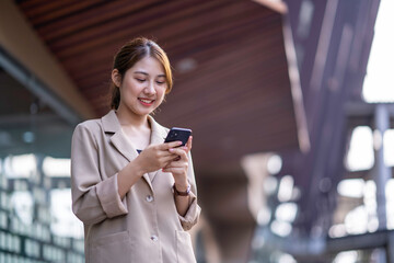 Beautiful cute Asian young businesswoman standing outside the cafe, using mobile phone and smiling