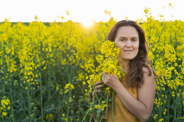 A girl in yellow. Woman with a bouquet of rapeseed flowers in the field