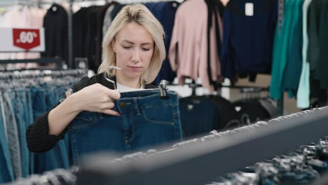 Elegant woman in a clothing store. The blonde chooses a new image for herself.