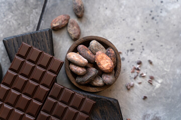 Stack of chocolate bars with cocoa beans. Flat lay composition with delicious chocolate on black background. Space for text