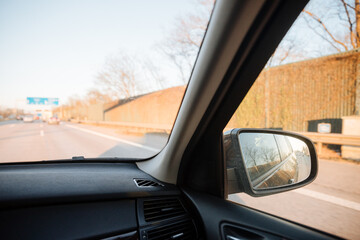Rearview mirror of a black car driving on a German autobahn. Safety and overtaking on fast highways 