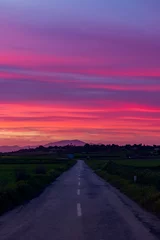 Fototapete Lila Kraftvoller hellroter und rosafarbener Sonnenuntergang über dem Feld mit Straße