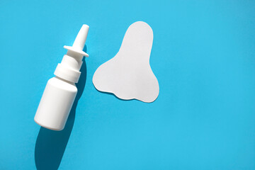 Paper silhouette of a nose and a can of spray on a blue background. Concept against allergic nasal congestion.