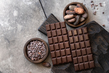 Stack of chocolate bars with cocoa beans. Flat lay composition with delicious chocolate on black background. Space for text