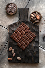 Stack of chocolate bars with cocoa beans. Flat lay composition with delicious chocolate on black background. Space for text