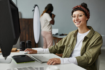 Portrait of smiling female photographer looking at camera while using computer at workplace in...