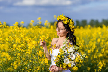 Portrait of a beautiful woman with a wreath of yellow flowers on her head. A girl with a bouquet in a rapeseed field collects flowers