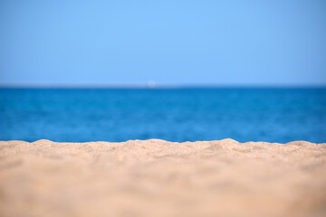 Obraz premium Close up of clean yellow sand surface covering seaside beach with blue sea water on background. Travel and vacations concept