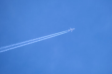 Distant passenger jet plane flying on high altitude on clear blue sky leaving white smoke trace of contrail behind. Air transportation concept