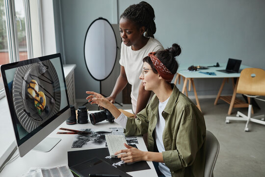 Side view portrait of two female photographers discussing images on computer screen while working on editing in studio