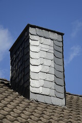 Chimney of Siegerland house with black slate shingles, clear blue winter sky, low angle view, concept: heating, fossil fuel, gas shortage, c02 footprint (vertical), Dahlbruch, NRW, Germany