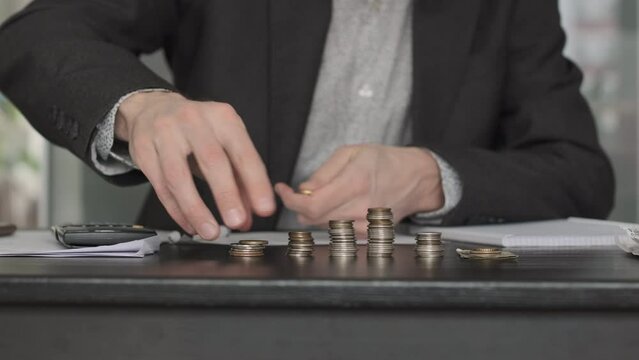Male Hand Stacking Coins and Counting on Table. Close up. He is Using Calculator and Taking Notes for Finance Accounting. Investment, Finance Management and Saving Money Concept