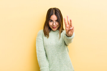 pretty hispanic woman smiling and looking friendly, showing number three or third with hand...