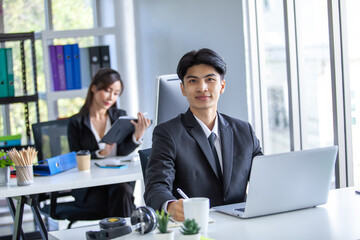 Portrait of Asian handsome man working at the office, using computer on table.