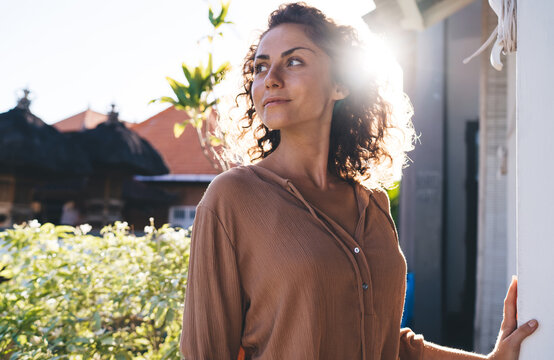 Contemplative female with curly hair thoughtful looking away thinking about weekend pastime during sunny vacations, pensive hipster girl dressed in casual wear spanding daytime outdoors