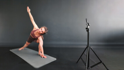 Fitness girl shows exercises master class via smartphone camera online. Fitness training remotely. The trainer records video on a smartphone. Fitness live. Online fitness classes.