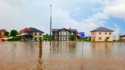Fototapeta na wymiar Extreme heavy rain storm weather. Flooded streets of the neighborhood. A flooded road junction with a drowned house. Heavy rains from tropical storm caused many flooded areas. Rains caused many floods