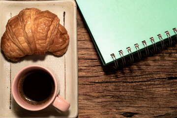 Breakfast food croissant in plate and coffee on wood table.