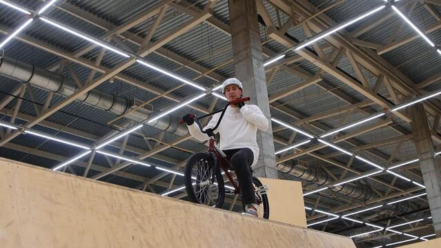 BMX sports - young man riding on the top of the springboard and takes off his helmet