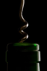 A wine bottle and a corkscrew against a black background
