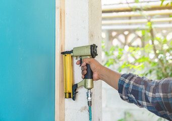 The carpenter with a air nail gun nailer working on wood frame.