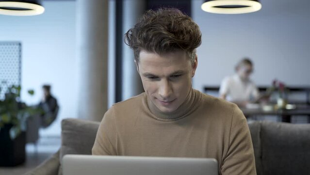 Young confident business freelance expert working in front of his laptop computer. Internet entrepreneur wearing casual outfit looks calm and focused on the work he is doing.