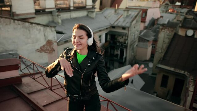 Slow motion of happy woman in wireless headphones dancing singing on a Roof at Sunset having fun alone
