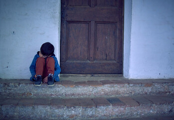 Melancholy Mixed Race Boy Sitting outside his house angry and sad with his head resting on his legs. horizontal, latino kid looking down