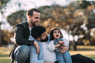 Gay couple enjoying in the park with their little daughter. Proud homosexual family concept.