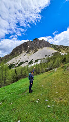 Fototapeta na wymiar Hiker woman with backpack on an alpine meadow in front of Hahnkogel (Klek) in Karawanks and Julian Alps, Carinthia, Austria. Border with Slovenia. Triglav National Park. Goal seeking. Hiking vacation
