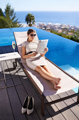 Enjoying her vacation. An attractive young woman reading a magazine while lying on a deck chair.