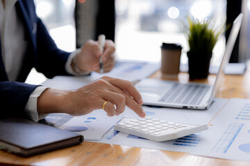 Close-up of a business man using a white calculator, a financial businessman examining the numerical data on a company financial document, he uses a calculator to verify the accuracy of numbers.