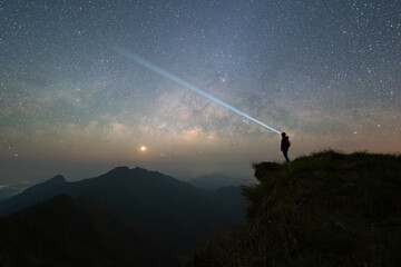 Portrait of Asian woman, a tourist, travel and use flash light at Chiang Rai, Thailand with mountain hills, the milky way in galaxy with stars at night. Universe space landscape. People lifestyle. - obrazy, fototapety, plakaty
