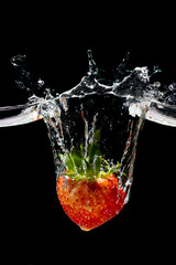 Red strawberry in water splash on black background.