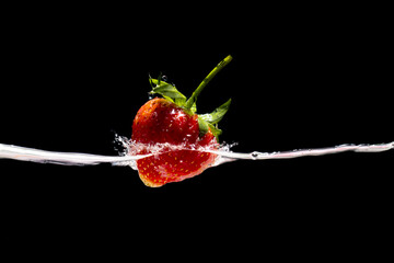 Red strawberry in water splash on black background.
