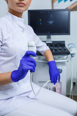 A young woman is an intern doctor, she is in a white suit and medical gloves holding an ultrasound probe on her hands. ultrasound diagnostics. selective focus