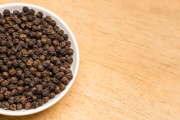 Close up of Black Pepper Seeds in a white bowl on wooden tray ( dried seeds of piper nigrum)