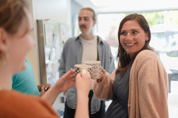 Happy friends toasting coffee mugs in kitchen