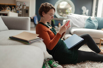 Young woman with laptop using smart phone in living room