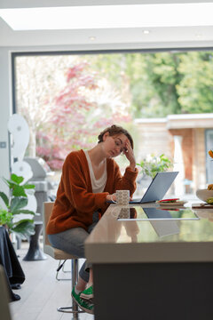 Stressed woman working from home at laptop in kitchen